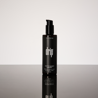 Black bottle labeled 'drip lubricant - water based' on a reflective surface with a light gray background