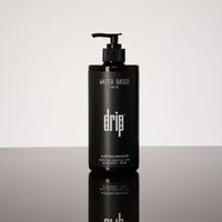 Black bottle labeled 'drip' on a reflective surface with a light gray background. drip water based lube.