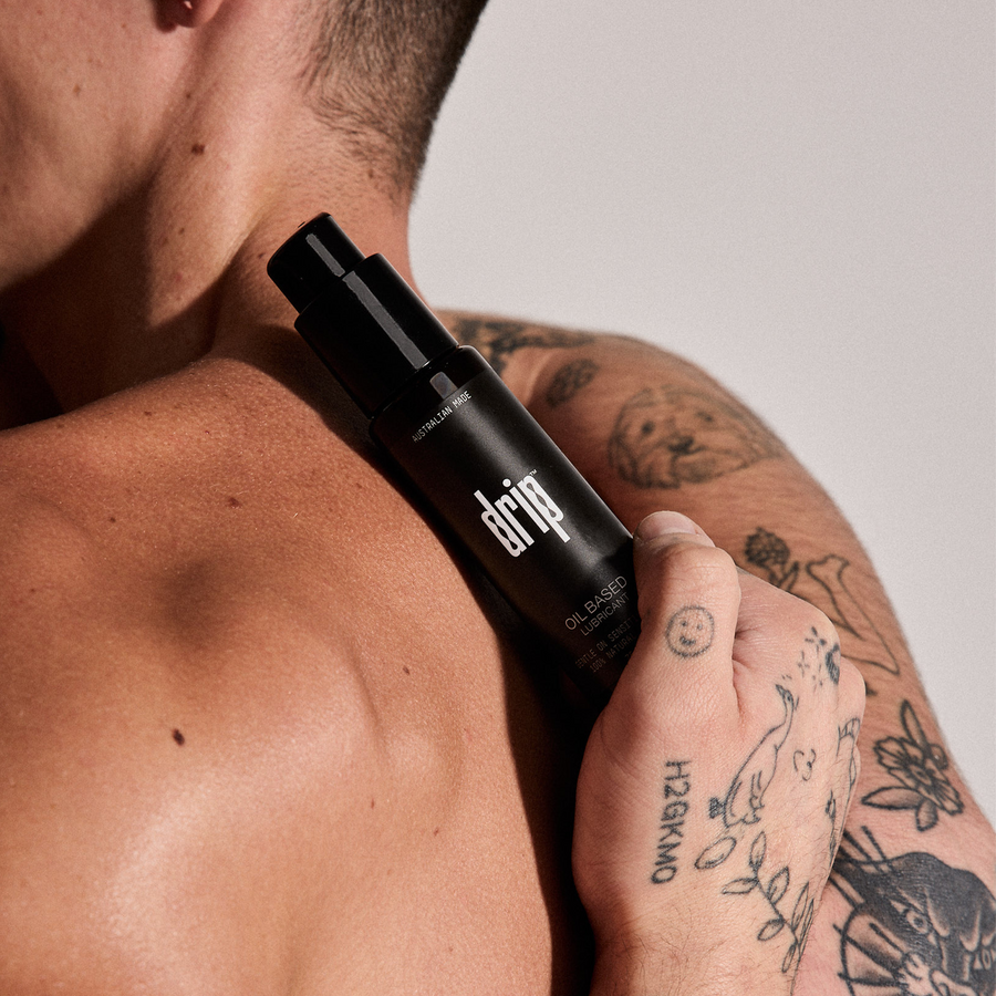 Person holding a black anal lube bottle labeled 'drip' against a neutral. Oil based lubricant.