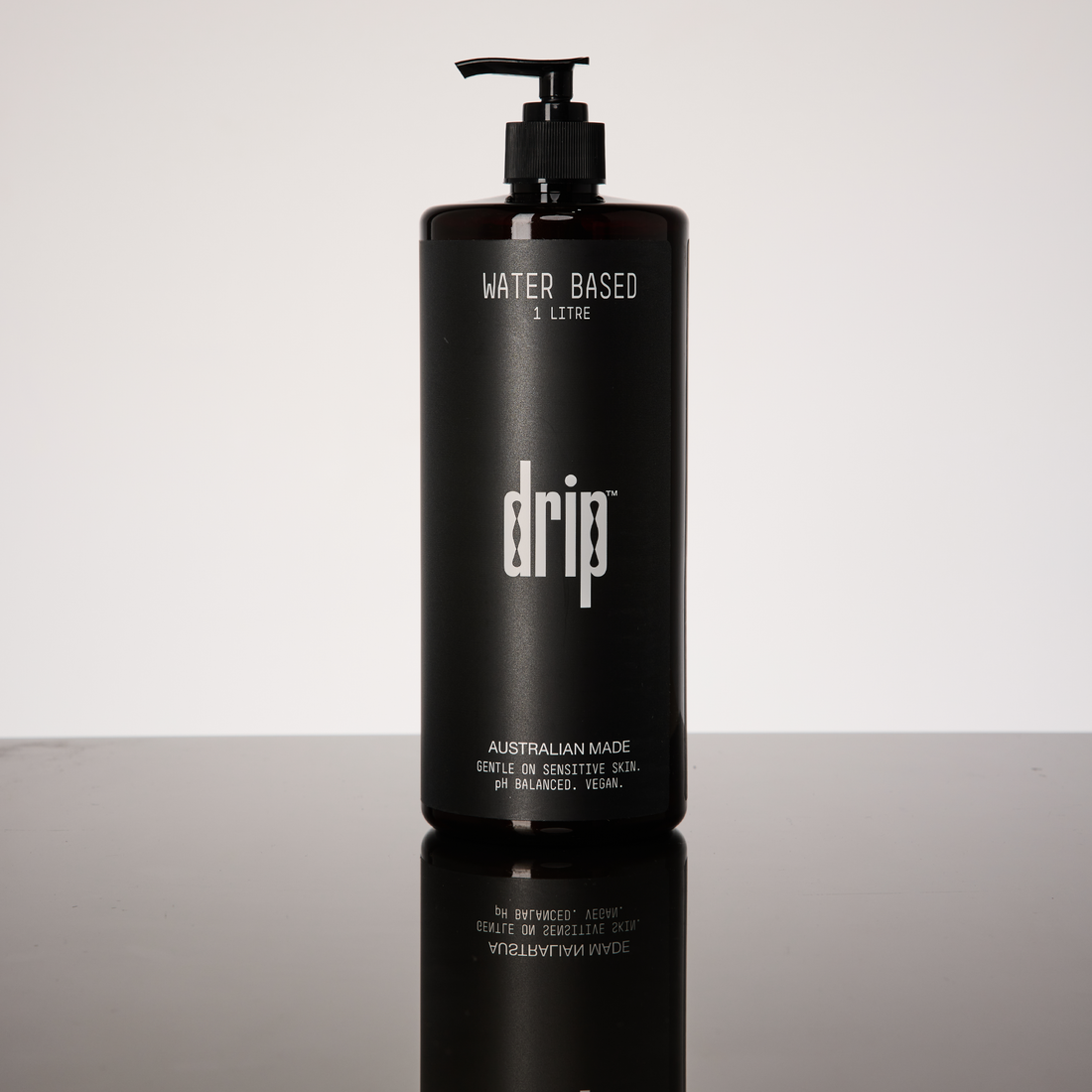 Black bottle labeled 'drip anal lube - water based' on a reflective surface with a light gray background