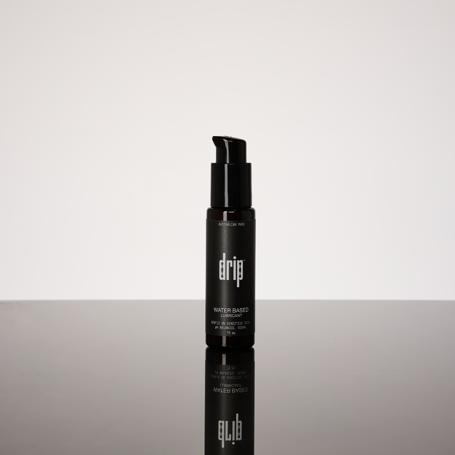 Black bottle labeled 'drip water based lubricant' on a reflective surface with a white background