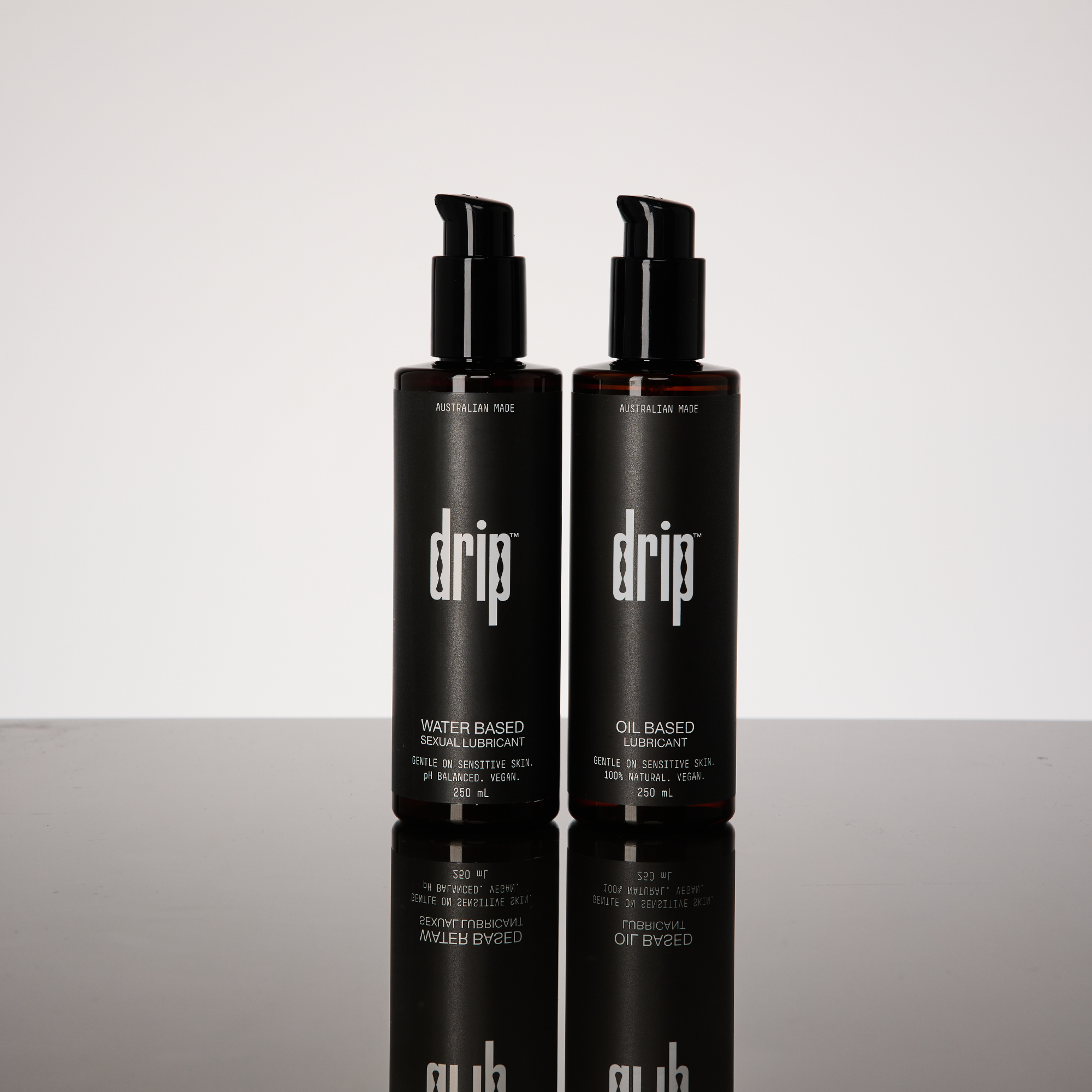 Two black 'drip' lubricant bottles on a reflective sexual anal lube.